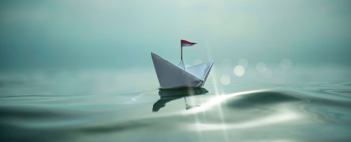 papierschiffchen-auf-ruhiger-blaugruener-see-mit-lichtreflexen
